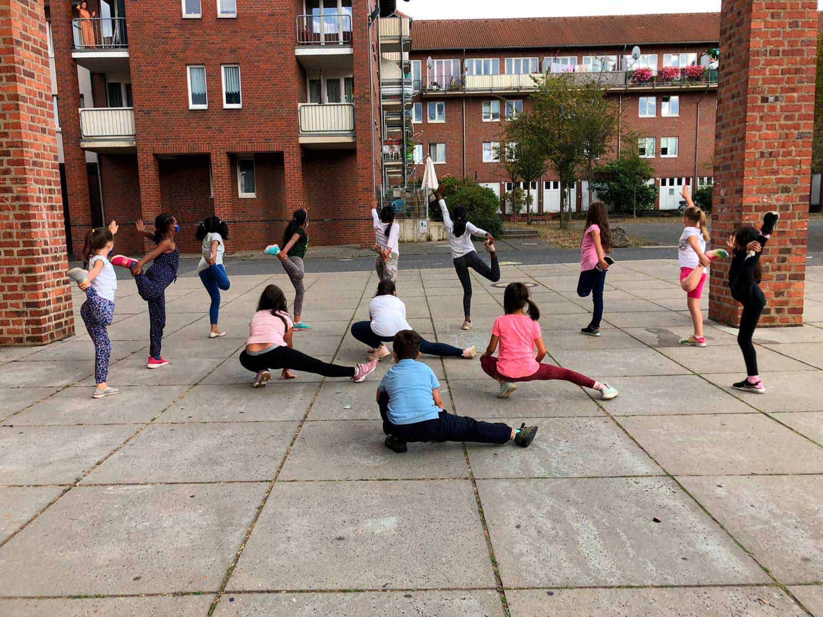 Kinder beim Yoga im Innenhof eines Mehrfamilienhauses in Berlin.